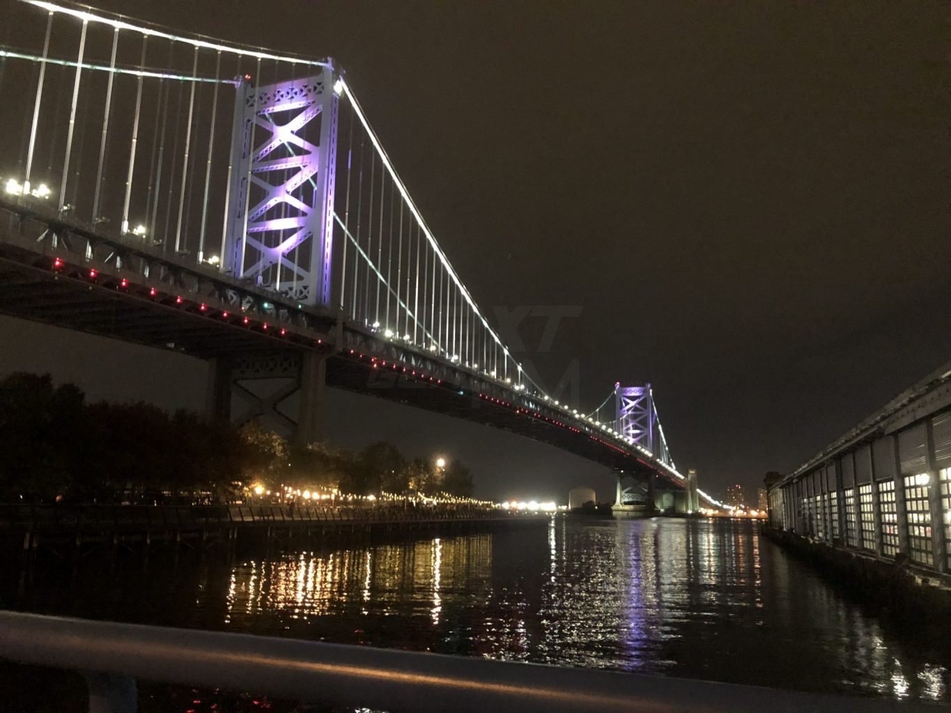 The Delaware River reflects the ghostly lights of the Ben Franklin Bridge.